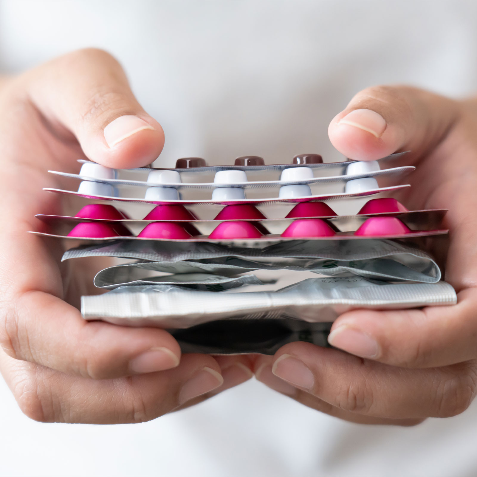 Hände halten einen Tabletten-Organizer mit pinken Kapseln und Blistern.